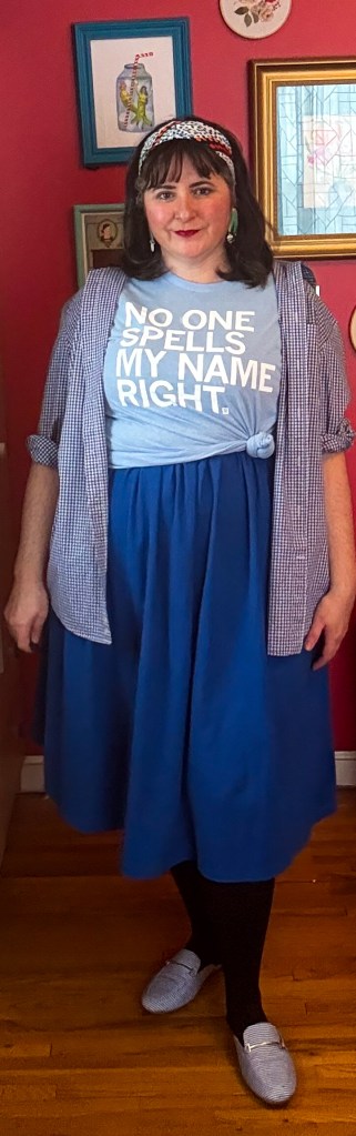 An all-blue outfit featuring a blue dress, a blue graphic t-shirt and a blue button-up. 